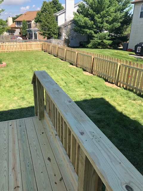 A wooden deck overlooking a fenced backyard with green grass and neighboring houses in the background.