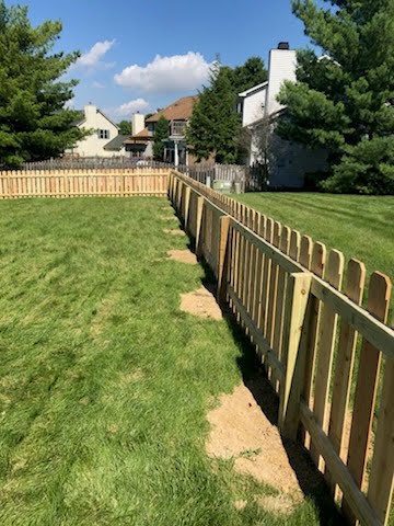 New wooden fence surrounding a grassy yard under a blue sky with scattered clouds.