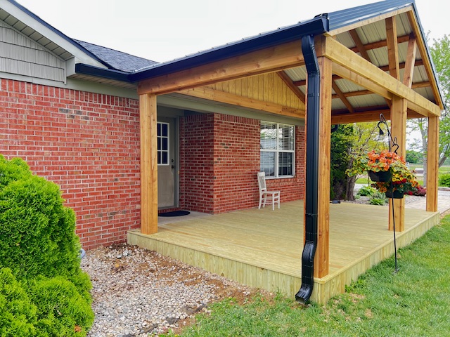 "Modern wooden patio with a covered structure, brick wall, and landscaping, offering a cozy outdoor space."