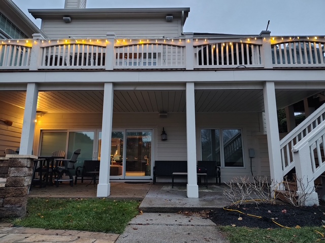 "Exterior view of a house’s lower patio with festive string lights, seating areas, and a landscaped yard."