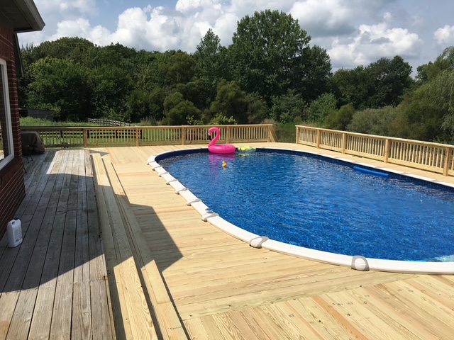 A sunny backyard with a swimming pool surrounded by wooden decking and a pink flamingo float.