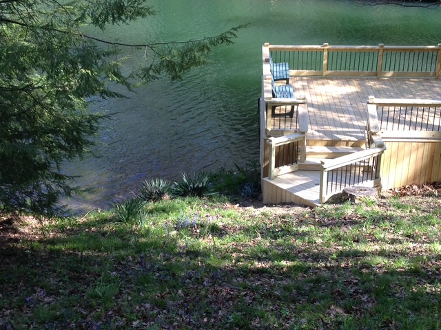 "Scenic riverside deck with wooden steps and a chair, surrounded by greenery and water."