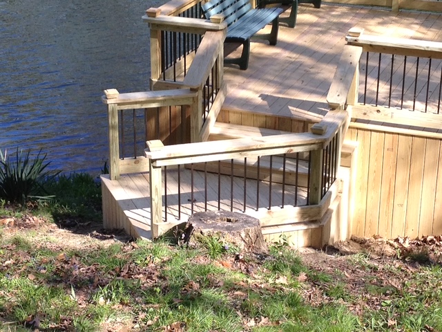 Wooden deck area near a body of water featuring a railing, a bench, and a small tree stump in the foreground.