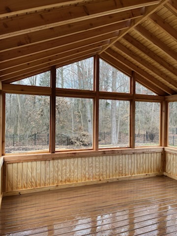 IMG_1188 Image of a newly constructed wooden sunroom with large windows and a sloped wooden ceiling, overlooking a natural outdoor setting.