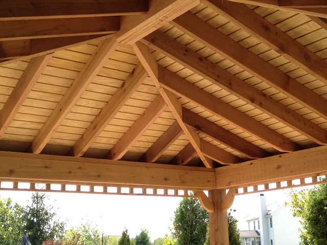 Wooden gazebo interior showcasing exposed beams and a sloped ceiling with natural light filtering through.