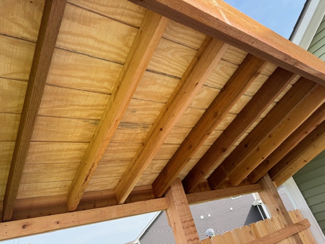 Underneath view of a wooden pergola showcasing the structural beams and ceiling panels.