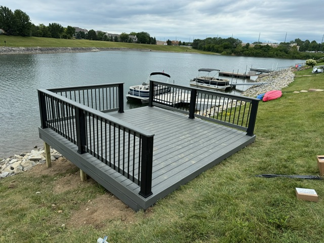 A newly constructed deck with black railings overlooking a calm lake and docked boats.