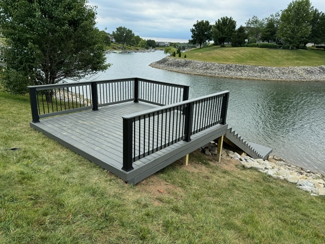 "Wooden deck overlooking a serene river with a grass landscape and steps leading down to the water."
