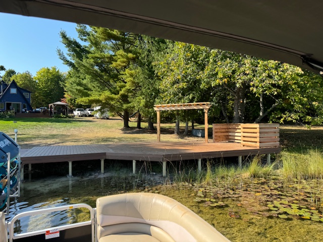 Scenic view of a wooden dock on a lake, with a grassy shore and trees in the background, ideal for relaxation and outdoor activities.