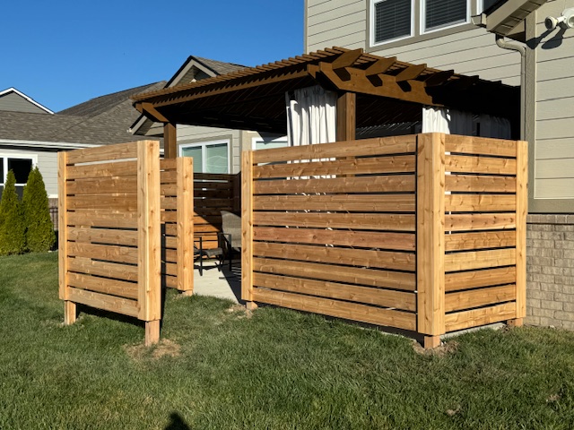 "Wooden slatted privacy fence enclosing a patio area with a pergola and outdoor seating."