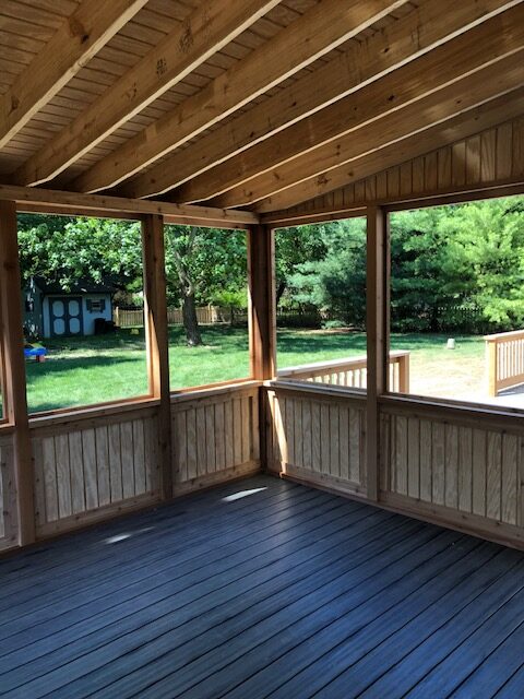 Open wooden screened porch with a view of a grassy backyard and trees.