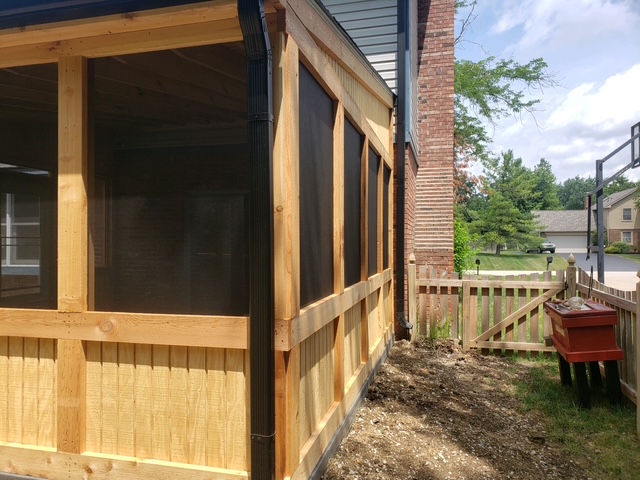 "Side view of a newly constructed wooden screened-in porch with natural wood finish, showcasing wire mesh and adjacent garden area."