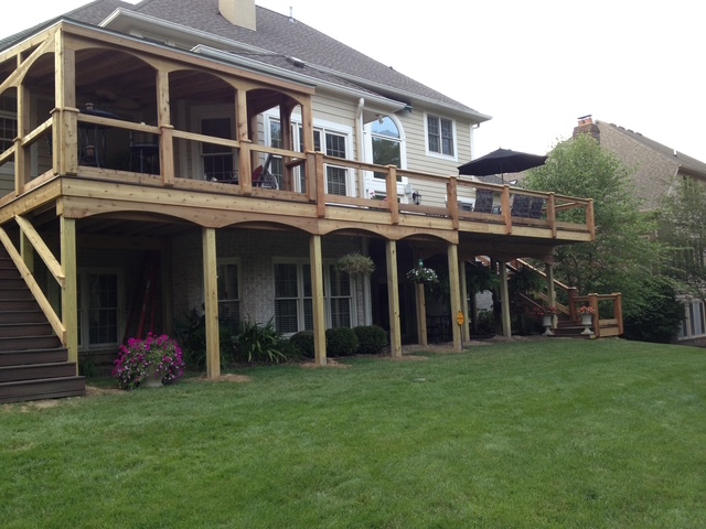 A wooden deck with a covered area and outdoor seating overlooks a well-maintained backyard and house.