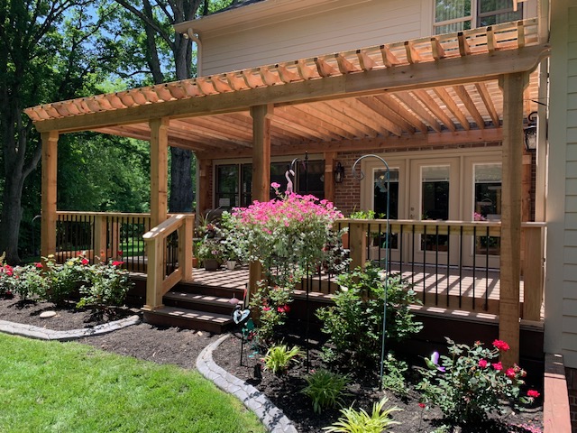 "Beautiful backyard patio with a wooden pergola, blooming flower beds, and lush green grass."