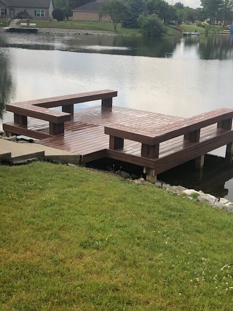 Wooden dock extending over a calm lake surrounded by grass and trees.