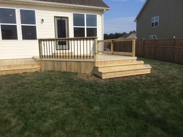 "Wooden deck with rails and steps leading to a white house, surrounded by a grassy yard and privacy fence."
