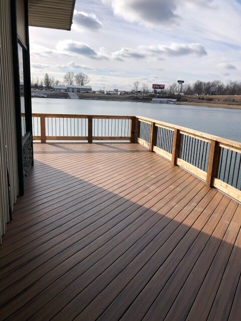 A wooden deck overlooking a calm lake with a cloudy sky in the background.