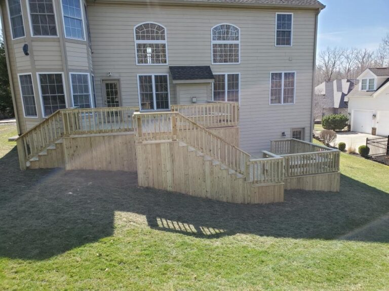 "Image of a two-story house with a newly constructed wooden deck and staircase leading to a grassy yard."