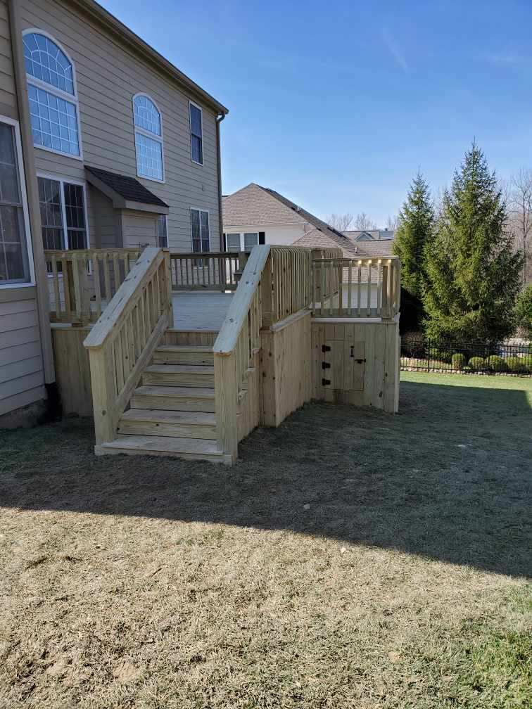 New wooden outdoor deck with stairs, attached to the side of a house, surrounded by a grassy yard.