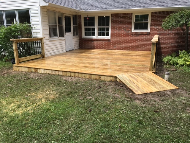 "Newly constructed wooden deck with a ramp and railing, extending from a home to a grassy area."
