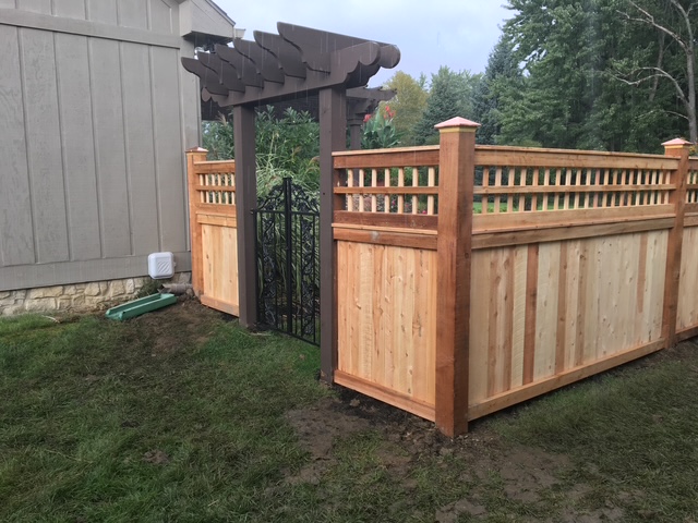 Wooden fence with decorative gate and pergola in a landscaped yard.