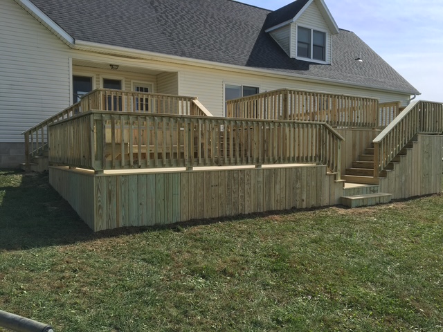 Newly constructed wooden deck with railings and stairs, attached to a house, showcasing a spacious outdoor area.