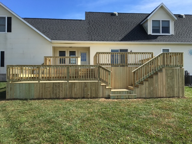 "Newly constructed wooden deck with stairs and railings attached to a white house under clear blue skies."
