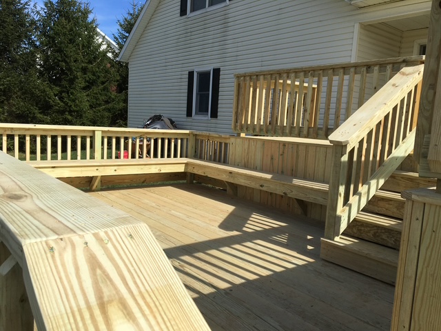 Newly constructed wooden deck with railing and stairs, situated beside a house, featuring a spacious design and natural light.