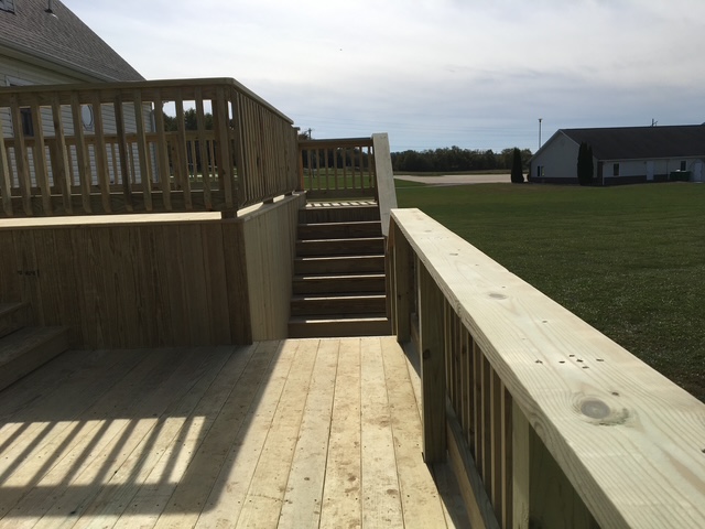 Image of a wooden deck with stairs leading down, surrounded by green grass and a cloudy sky in the background.