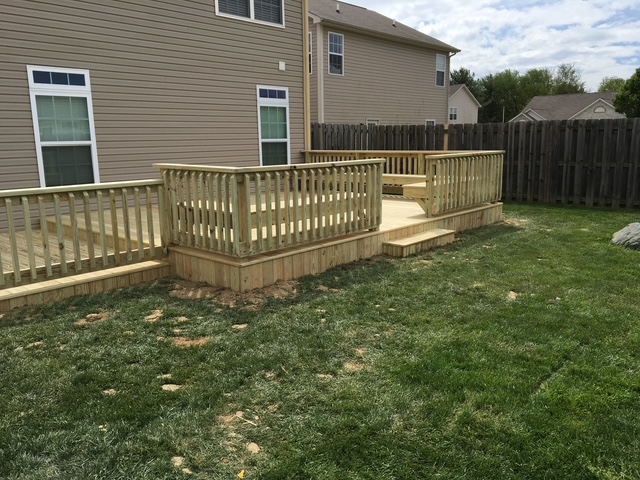 "Wooden deck with railings in a residential backyard, featuring steps and green grass."