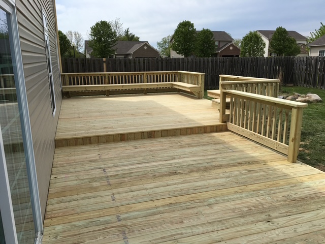 "Spacious wooden deck with railings, surrounded by green grass and trees, under a cloudy sky."