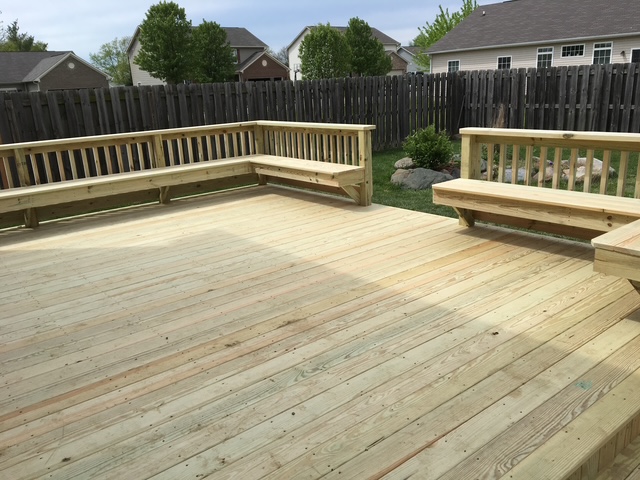 "Spacious wooden deck with built-in seating and a fenced backyard."