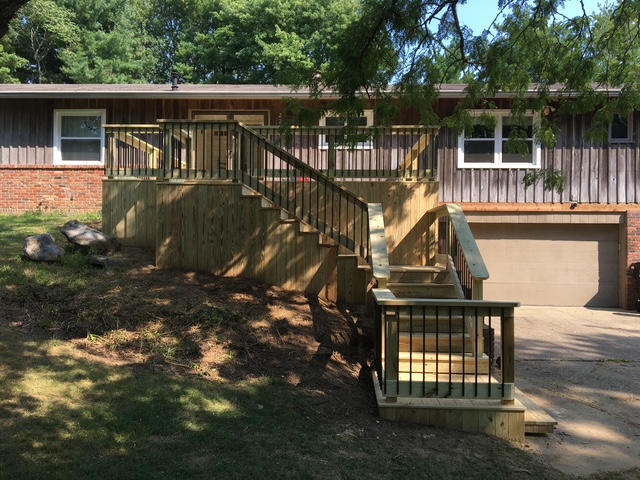 "Wooden staircase with railings leading to a house, surrounded by greenery."