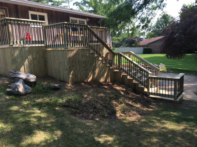 "Wooden deck with black railing and staircase leading to a landscaped yard."
