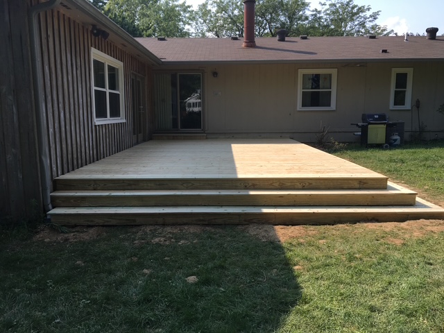 Newly constructed wooden deck with steps extending from a house, surrounded by grass.