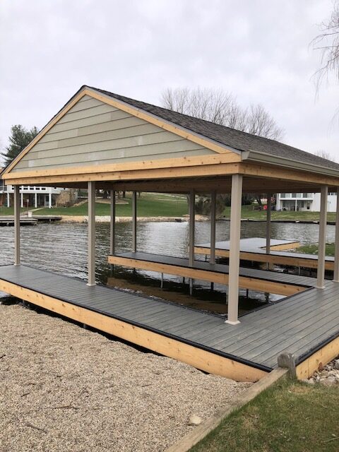 Pavilion over a wooden dock by a calm lake, surrounded by lawns and trees.