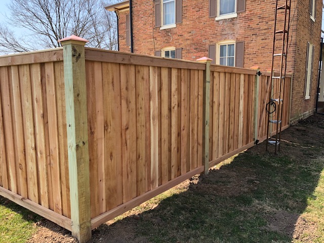 Newly installed wooden fence with a natural finish, bordering a well-maintained lawn near a brick building.