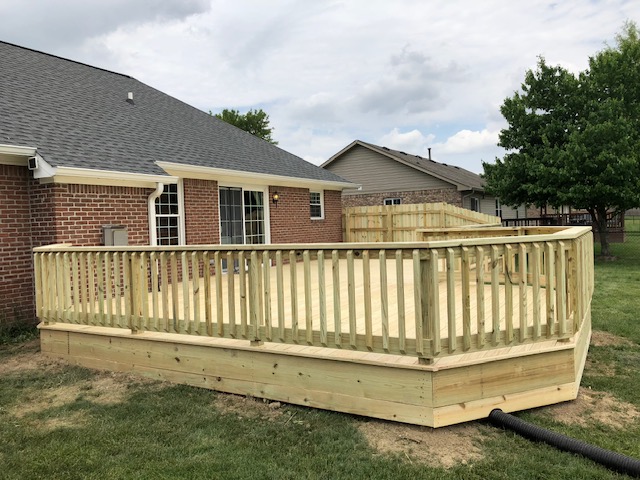 Newly constructed wooden deck with a railing, adjacent to a brick house in a residential backyard.