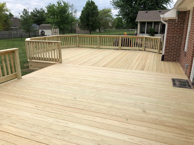 Newly constructed wooden deck with a railing, set in a grassy backyard, showcasing ample space for outdoor activities.