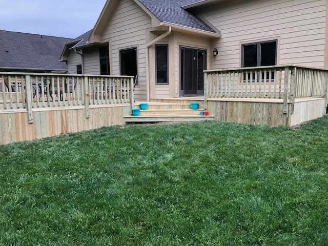 "Backyard view of a house with a wooden deck, fenced area, and neatly trimmed grass."