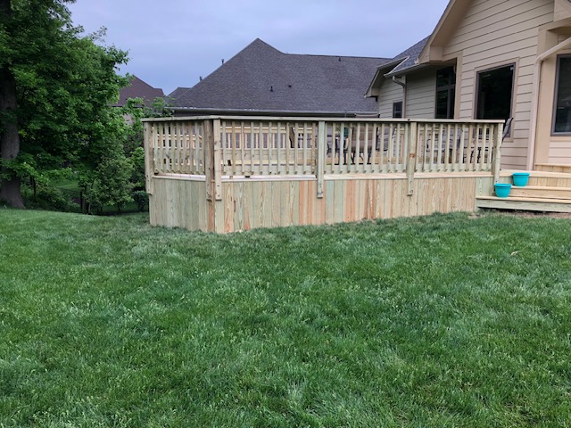 A wooden deck enclosed with railing, situated in a grassy backyard next to a house.