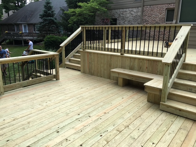 "Custom wooden deck with railings, stairs, and built-in seating in a landscaped backyard."