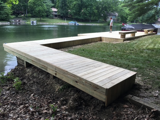 A newly constructed wooden dock extends into a lake, featuring benches and a clear view of the surrounding greenery.