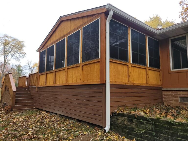 Resized_20221026_144552_741723752170439 A well-constructed screened-in porch with a wooden exterior, featuring a sloped roof and steps leading up, surrounded by autumn leaves.