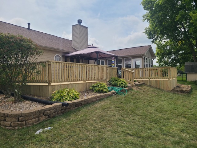 A wooden deck and patio with an umbrella, surrounded by landscaped vegetation, adjacent to a house in a grassy outdoor setting.
