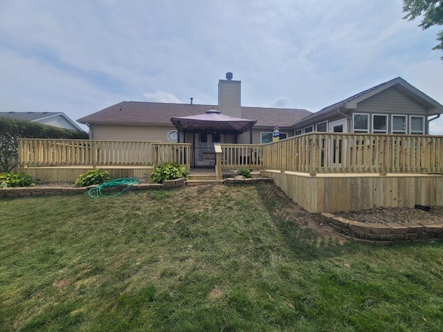 A backyard view of a house featuring a newly built wooden deck with a purple umbrella and landscaped greenery.