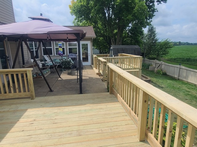 "View of a wooden deck with a gazebo and seating area, surrounded by greenery and a fenced yard."