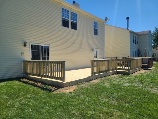 "Deck built in a backyard with two-story house in the background under clear blue skies."