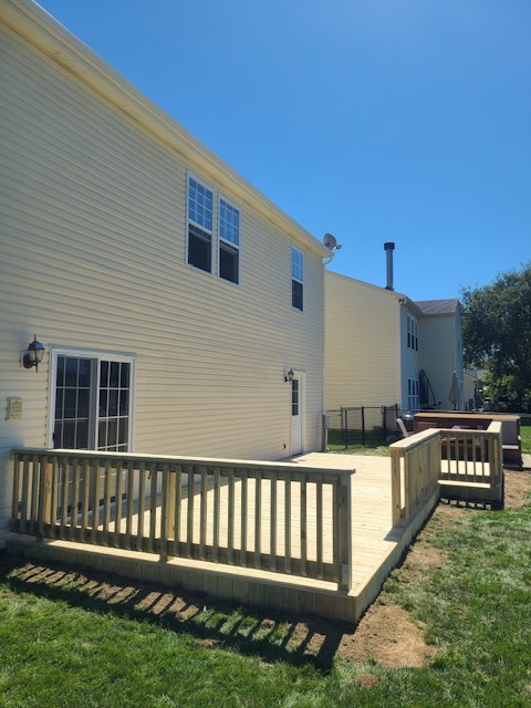 Well-constructed wooden deck in a sunny backyard, featuring a railing, adjacent to a light yellow house with multiple windows.
