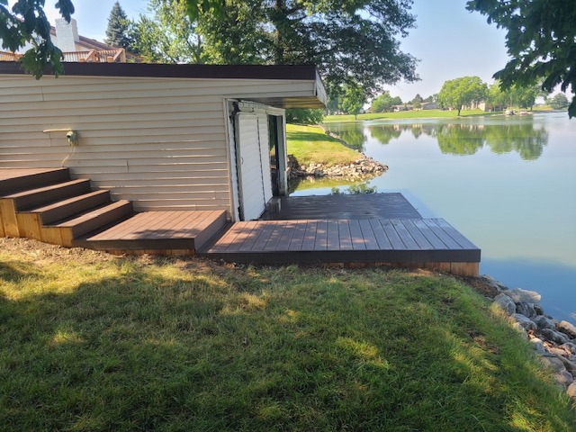 A modern wooden deck adjacent to a lakeside building, with steps leading to a serene waterfront view.